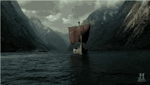 a boat with a red sail is floating in a river with mountains in the background