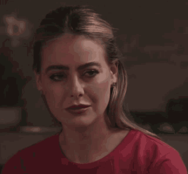 a woman in a red t-shirt is looking at the camera