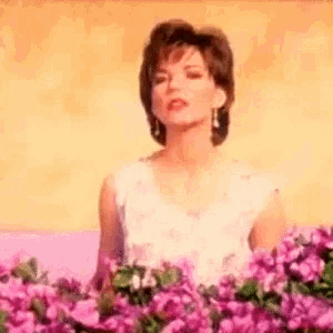 a woman in a white dress is standing in front of a field of pink flowers .