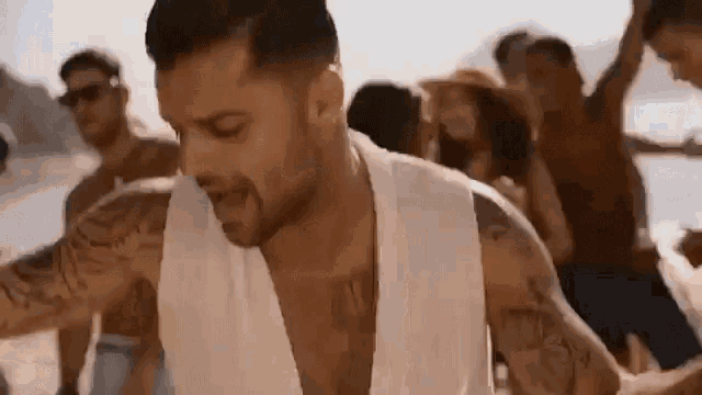 a man with a tattoo on his arm is dancing on the beach with a group of people .