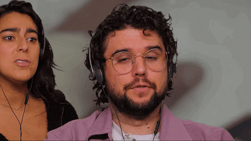 a man with glasses and a beard is wearing headphones while a woman looks on