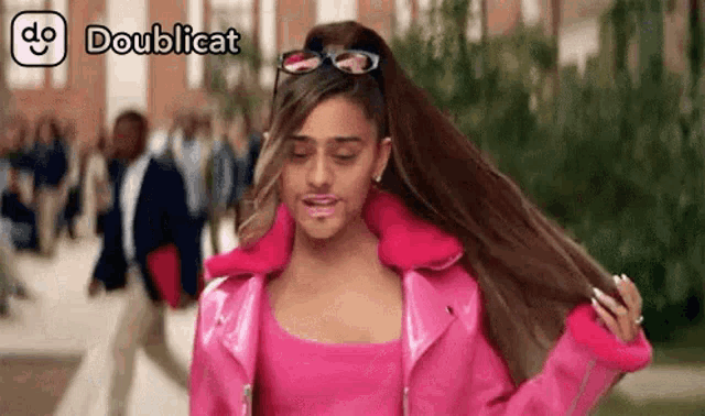 a woman in a pink jacket is holding her hair in a ponytail .