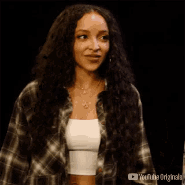 a woman wearing a plaid shirt and a white tank top is saying thank you .