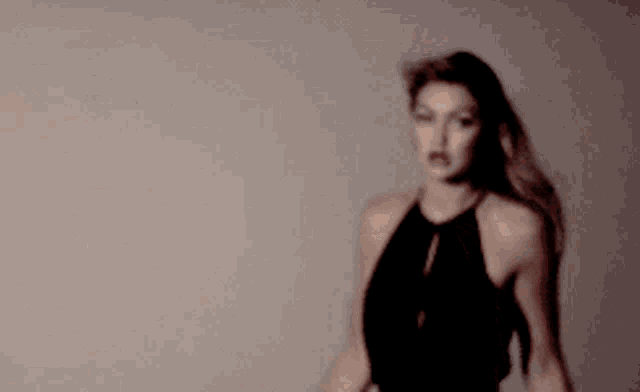 a woman in a black dress with her hair blowing in the wind is looking at the camera