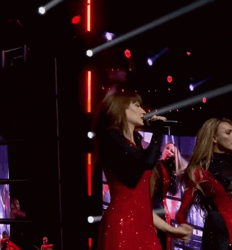 two women in red dresses are singing into microphones on stage