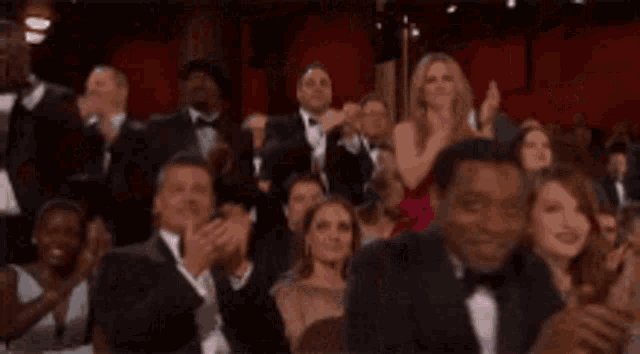 a man in a tuxedo stands in front of a crowd with the words isaac & the guys when the boobs come out