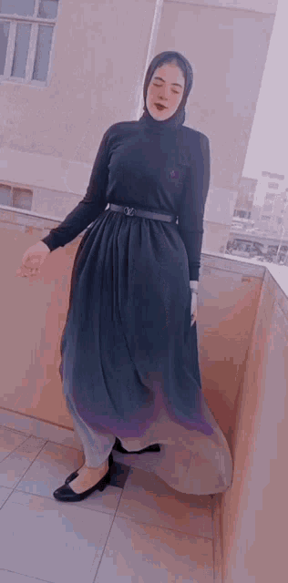 a woman wearing a hijab and a black dress is standing on a balcony