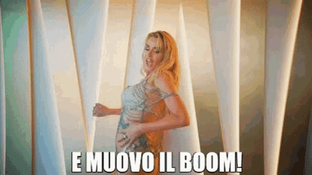 a woman in a dress is dancing in front of a wall with the words e muovo il boom written below her .