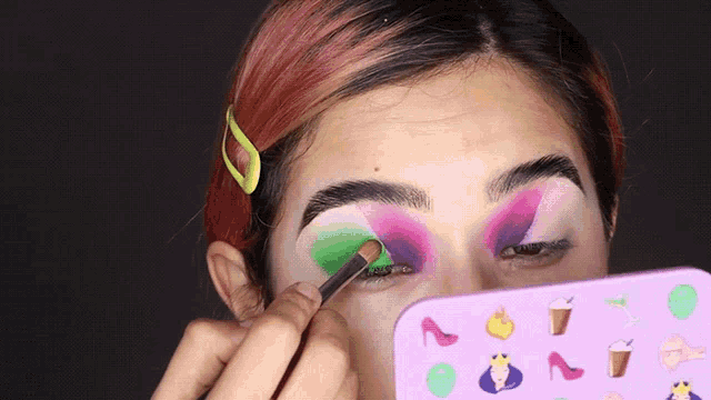 a woman is applying makeup with a purple and green eye shadow