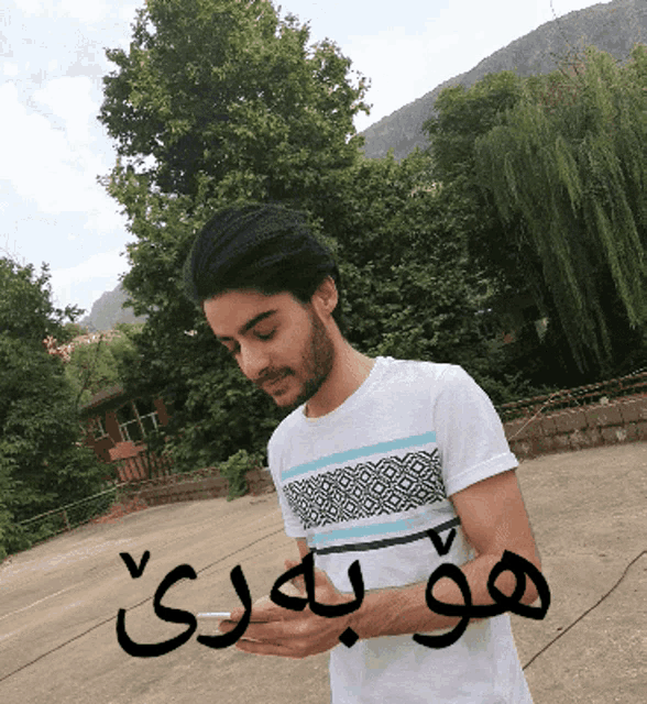 a man in a white t-shirt is looking at his cell phone with arabic writing on the ground behind him