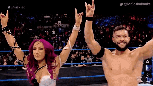 a man and a woman are standing next to each other in a wrestling ring with their arms in the air .