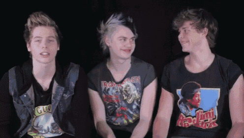 a man wearing an iron maiden shirt sits next to two other men