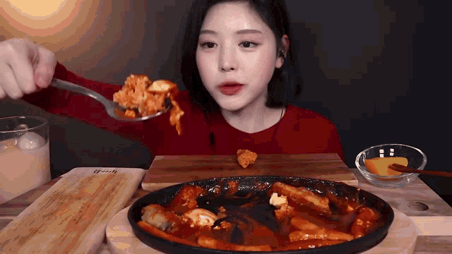 a woman in a red sweater is eating a spoonful of food