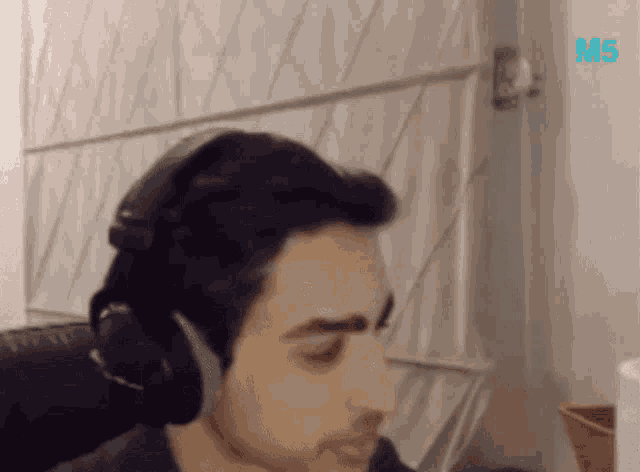 a man wearing headphones is sitting in front of a wall with the word m5 written on it