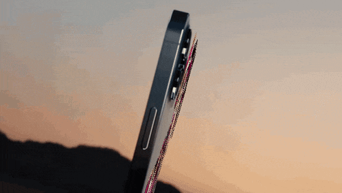 a close up of a cell phone against a sunset sky with mountains in the background