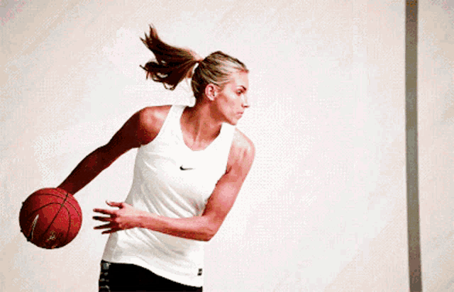a woman in a white nike tank top is holding a basketball
