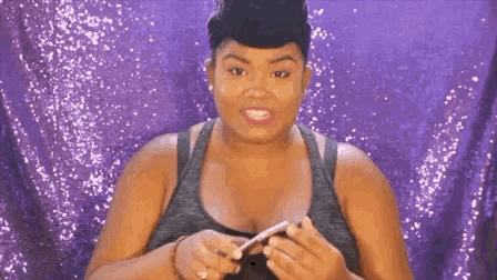 a woman is holding a cell phone in her hands in front of a purple background .
