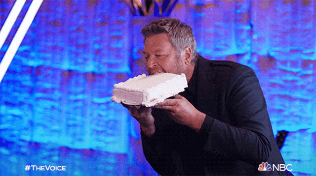 a man in a suit is eating a cake with the nbc logo on the bottom right