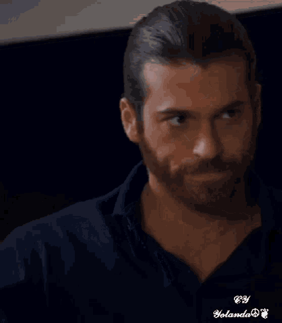 a man with long hair and a beard wearing a blue shirt is smiling .