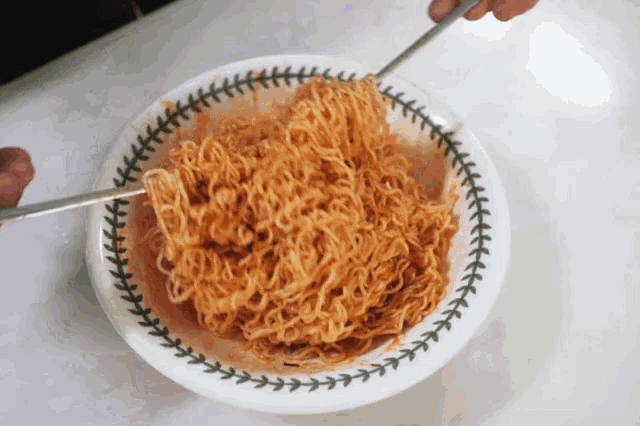 a bowl of noodles is being stirred with a pair of chopsticks