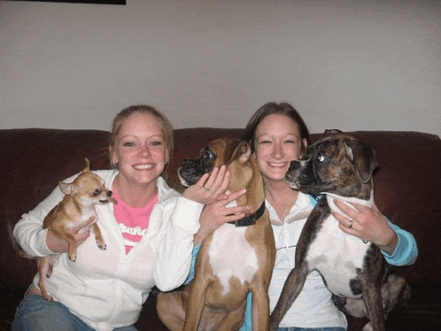 two women sitting on a couch with their boxer dogs