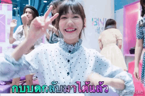 a girl in a blue polka dot shirt is smiling and giving a peace sign