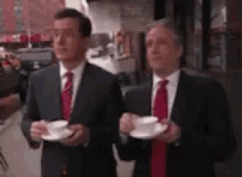 two men in suits and ties are holding cups of coffee .