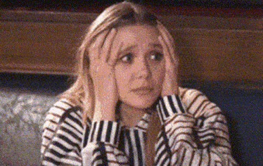 a woman in a striped shirt is sitting on a couch holding her head with her hands .