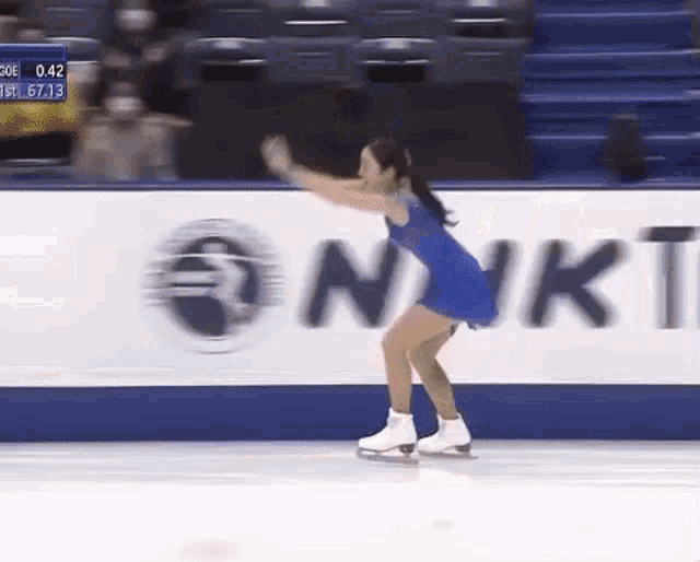 a woman in a blue dress is ice skating on a rink in front of a sign that says nkt .