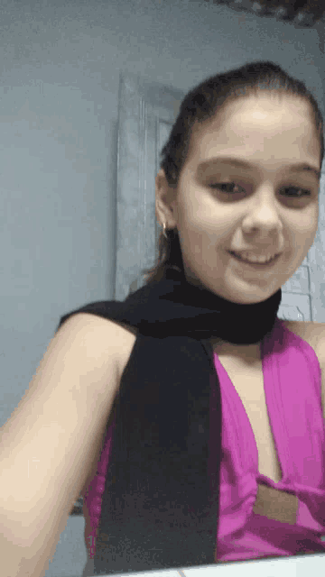 a girl wearing a black scarf and a purple top smiles for the camera