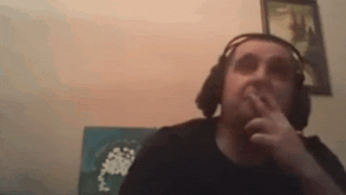 a man wearing headphones is smoking a cigarette while sitting in front of a wall .