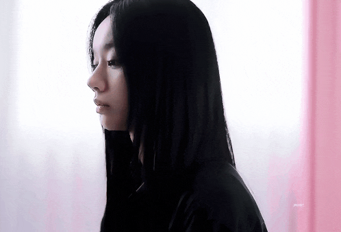 a woman with long black hair is standing in front of a pink wall