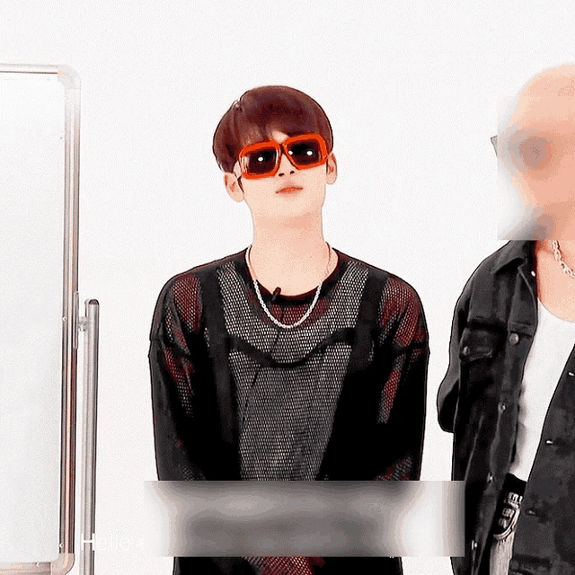 a man wearing sunglasses and a necklace is standing next to another man