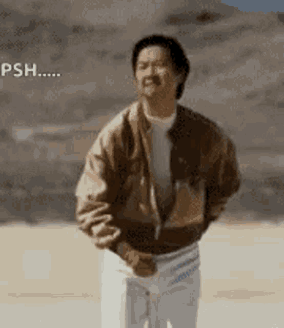 a man in a brown jacket and white pants is standing in the desert with his hands in his pockets .