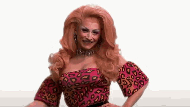 a drag queen with red hair is wearing a leopard print top and a necklace .