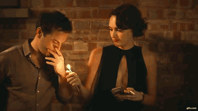 a man is lighting a cigarette while a woman looks at her cell phone