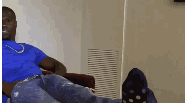 a man in a blue shirt is laying on a couch with his legs crossed
