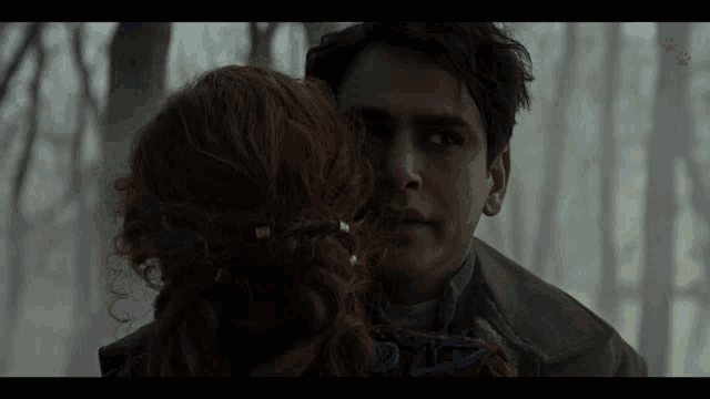 a man and a woman are looking at each other in a dark forest