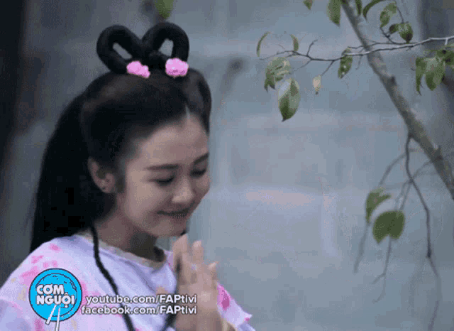 a girl with a bow in her hair is smiling in front of a tree branch with com người written on the bottom right