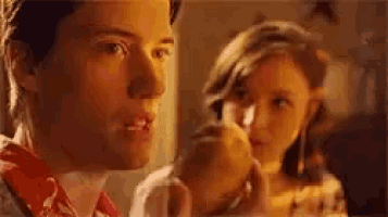 a man and a woman are looking at each other in a room . the man is holding an apple in his hand .