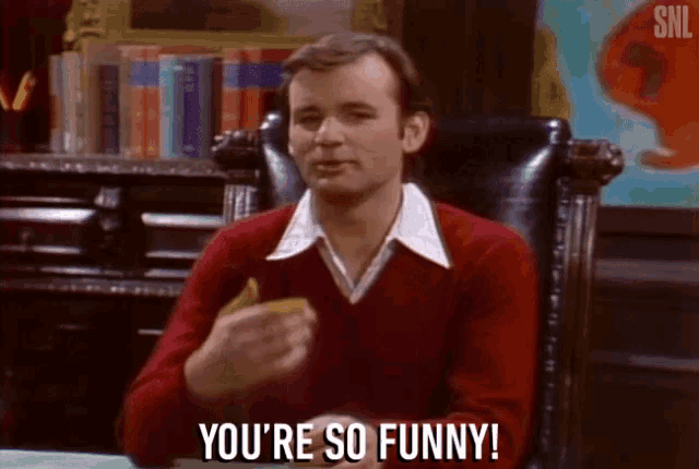 a man in a red sweater says " you 're so funny " while eating a sandwich
