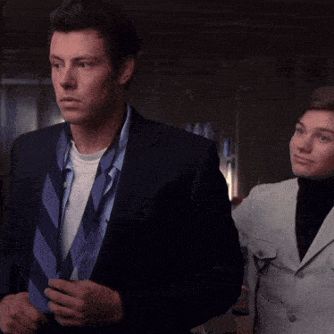 a man in a suit adjusts his tie while standing next to a woman in a white coat