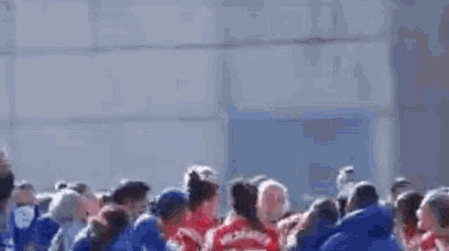 a group of people in blue jackets are standing in a circle holding hands .