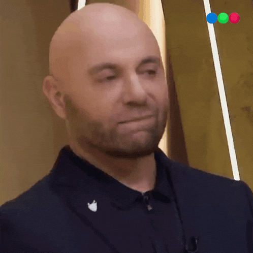a bald man with a beard is wearing a black suit and a black shirt .
