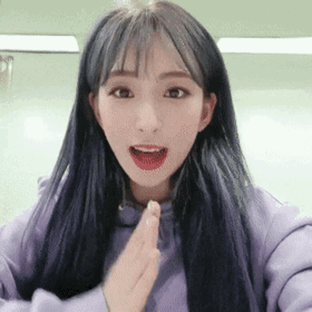 a girl with long blue hair and bangs is wearing a purple sweatshirt