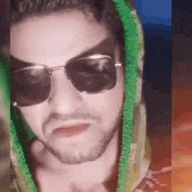 a man wearing sunglasses and a green hoodie is making a face
