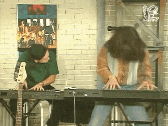 a man playing a keyboard next to a woman playing a guitar in front of a brick wall