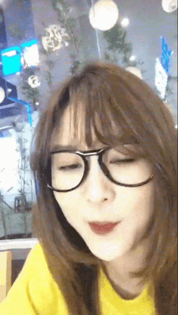 a woman wearing glasses and a yellow shirt looks at the camera