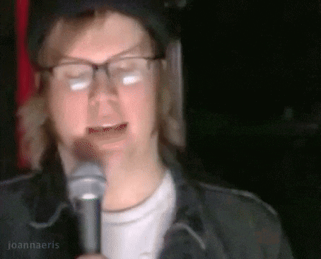 a man wearing glasses is singing into a microphone and the name joannaeris is on the bottom right