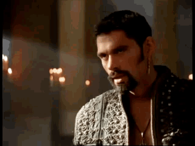 a man with a beard wearing a black jacket and earrings